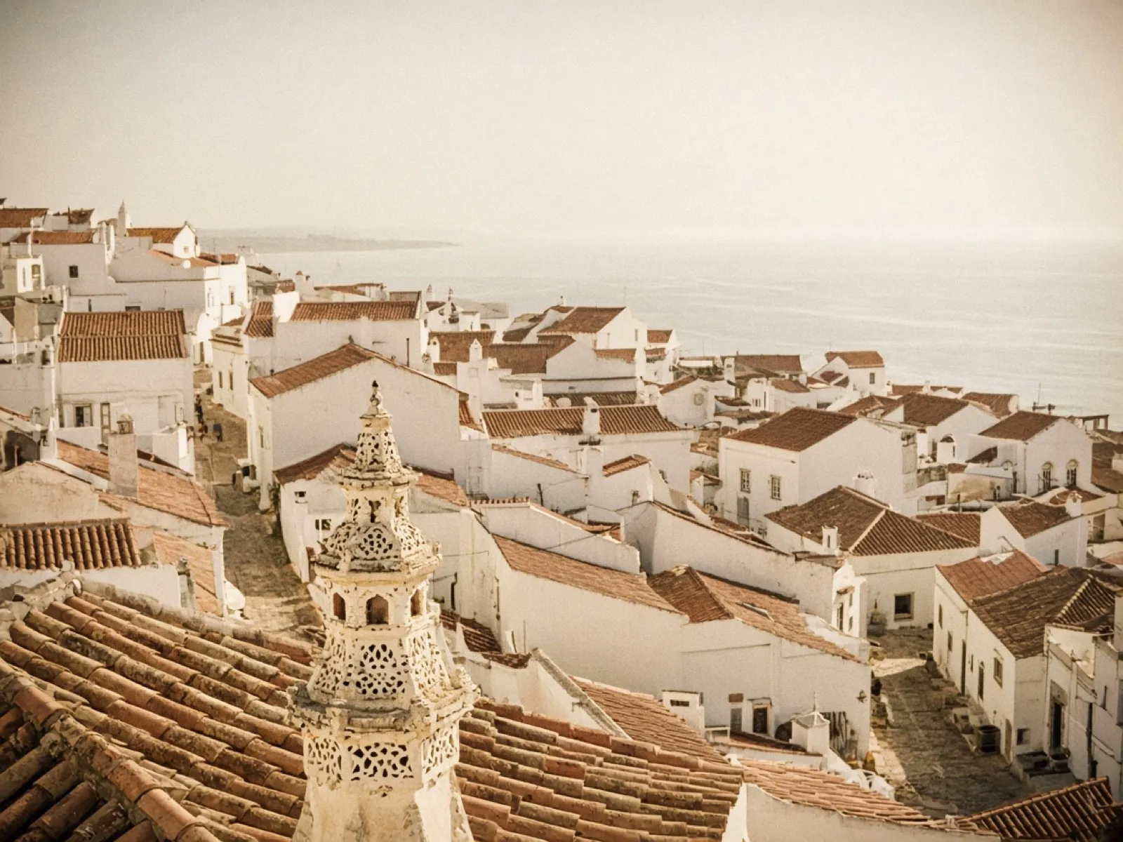 Whitewashed rooftops of an Algarve hill town above a hazy sea